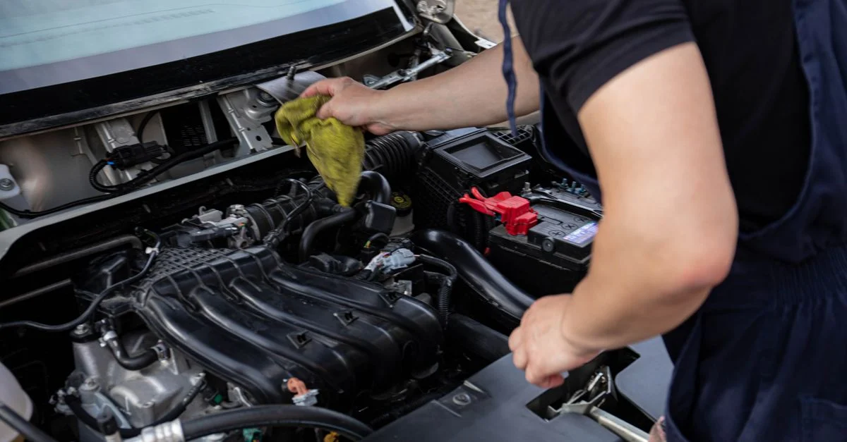 Gros plan d'un mécanicien réparant un moteur de voiture, axé sur l'entretien et le nettoyage.